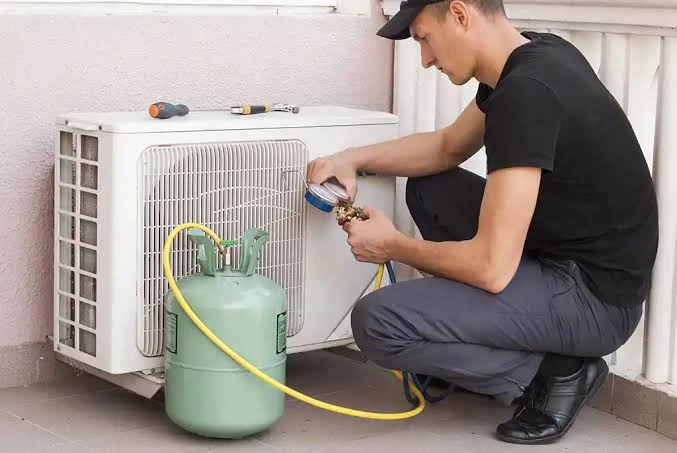Technician checking refrigerant pressure beside a residential air conditioner
